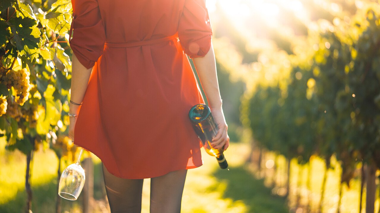 donna_vestito_rosso_tra_vigne_con_bicchiere_bottiglia_picjumbo_viktor_hanacek