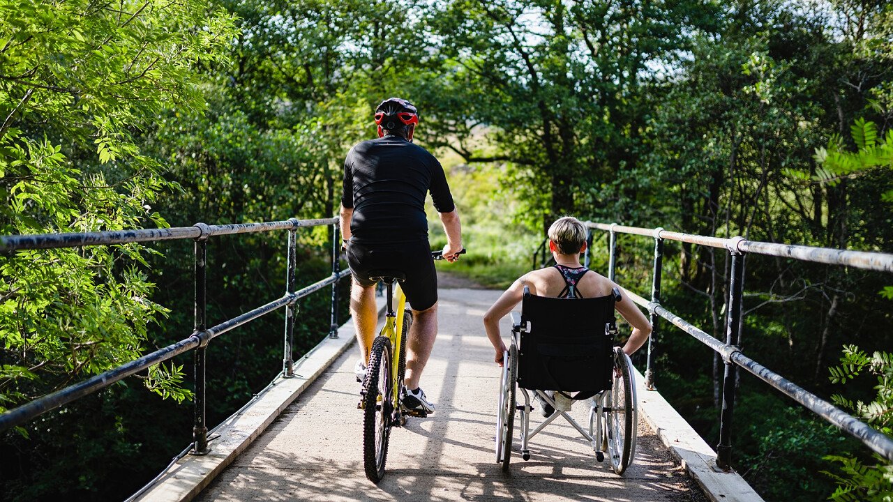 Person auf einem Fahrrad mit einer Person im Rollstuhl neben sich