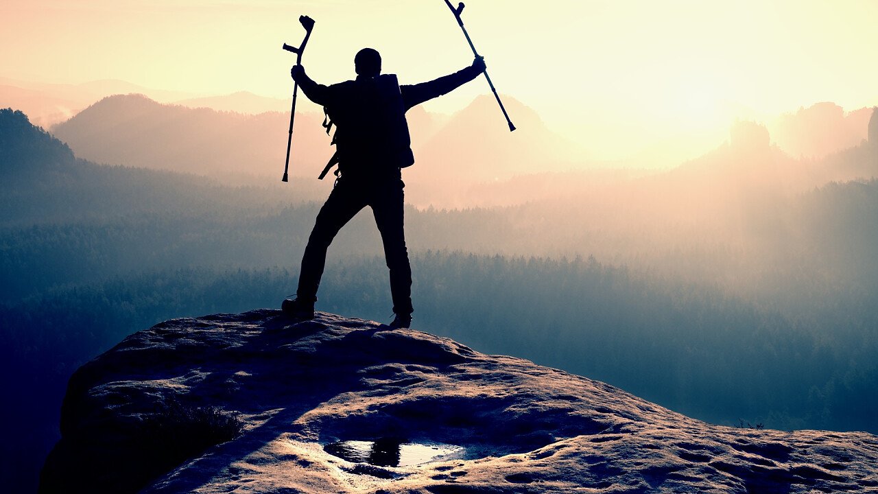 Person mit Krücken auf dem Gipfel des Berges